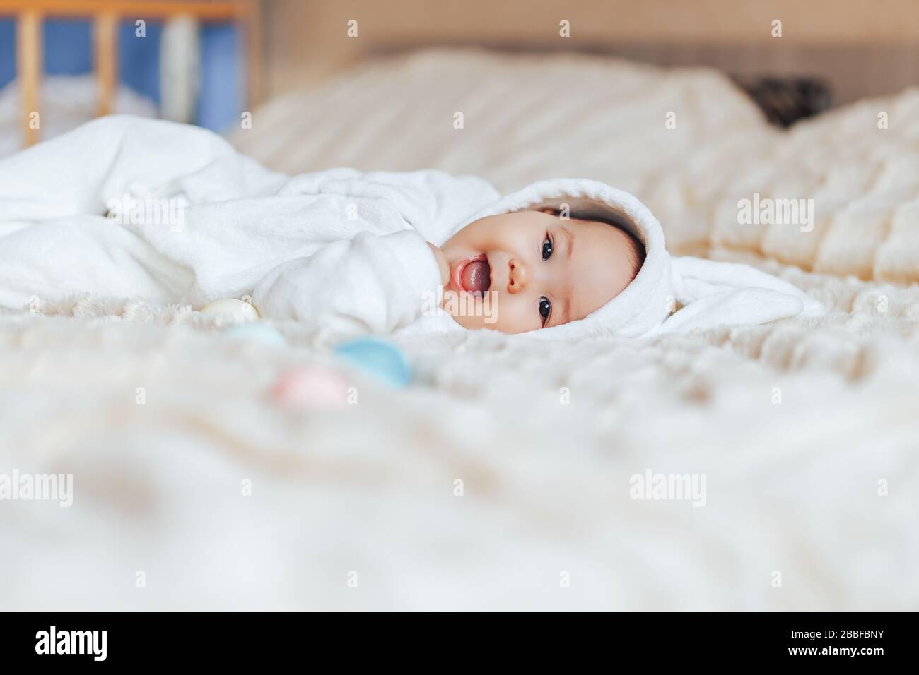 Joli sourire heureux petit bébé en costume blanc de lapin, jouant avec des œufs de pâques colorés Banque D'Images