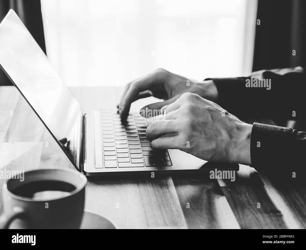 Un homme est en train de taper sur un clavier d'ordinateur portable. Concept de travail à domicile, photo en noir et blanc. Banque D'Images