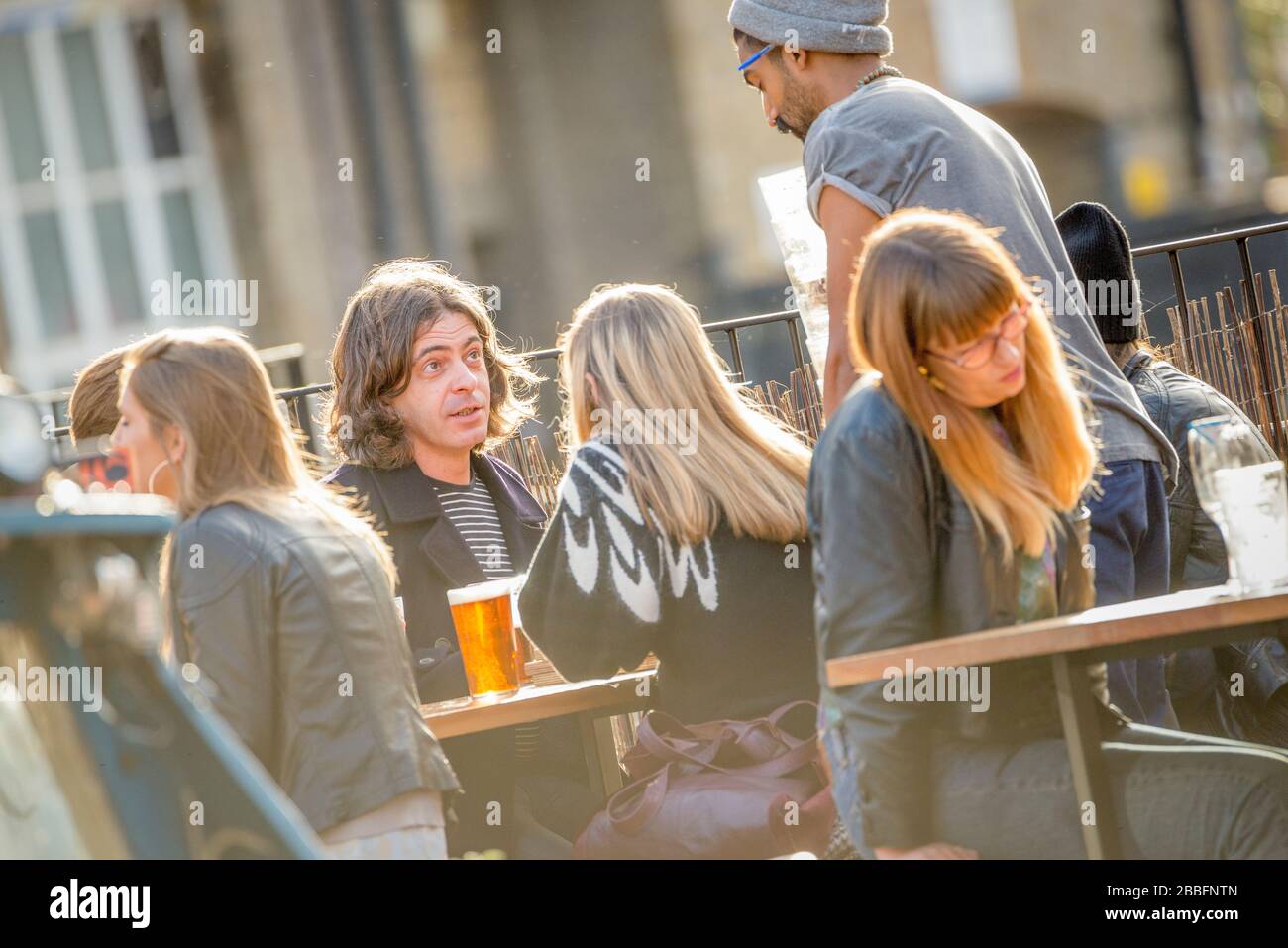 Dîner au soleil sur un serveur en train de prendre des verres sur la terrasse d'un bar est de Londres cool et animé à Hackney Wick. Banque D'Images