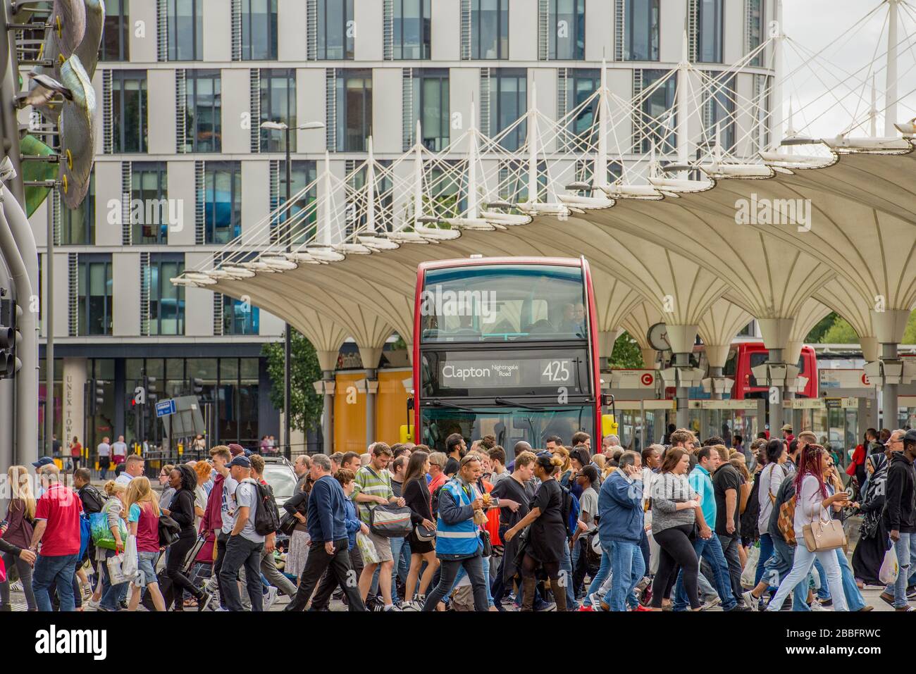 Des foules de clients traversent la rue entre la gare de Stratford et le centre commercial Stratford Center pendant une journée estivale ensoleillée. Un bus londonien attend. Banque D'Images
