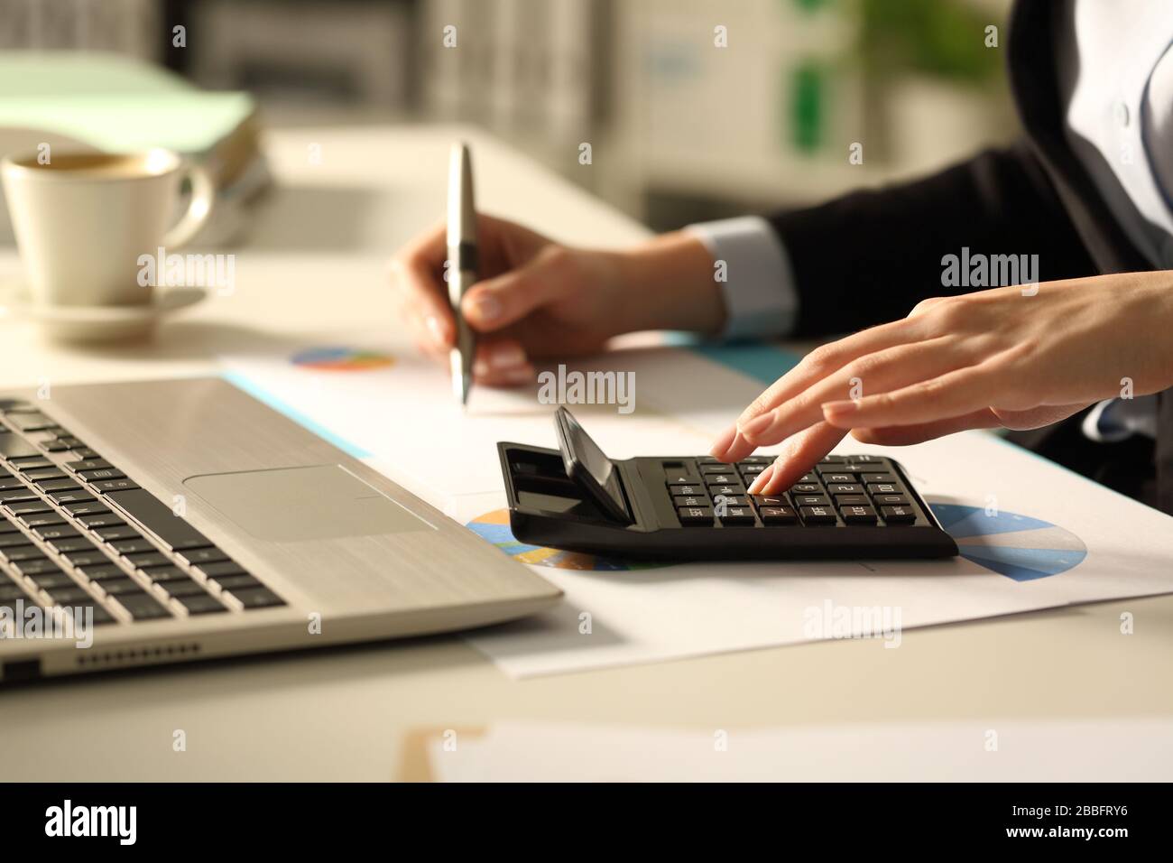 Gros plan sur les mains de la femme exécutive calculant avec calculatrice la nuit sur un bureau au bureau Banque D'Images