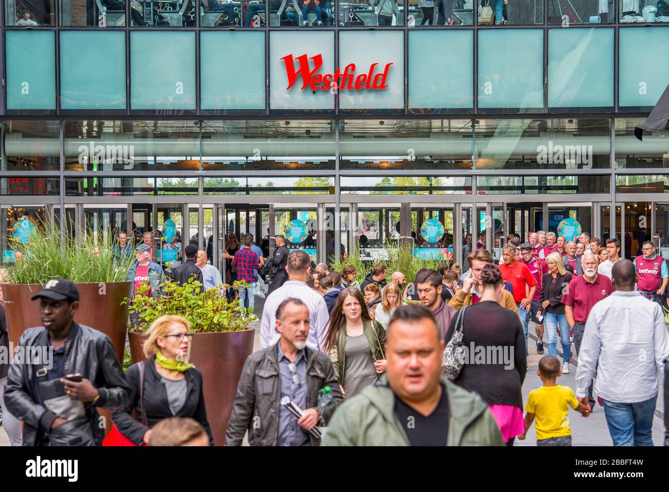 Une journée d'été très animée au Westfield Shopping Mall dans East London Shoppers remplir l'une des entrées du centre avec la marque au-dessus des portes. Banque D'Images