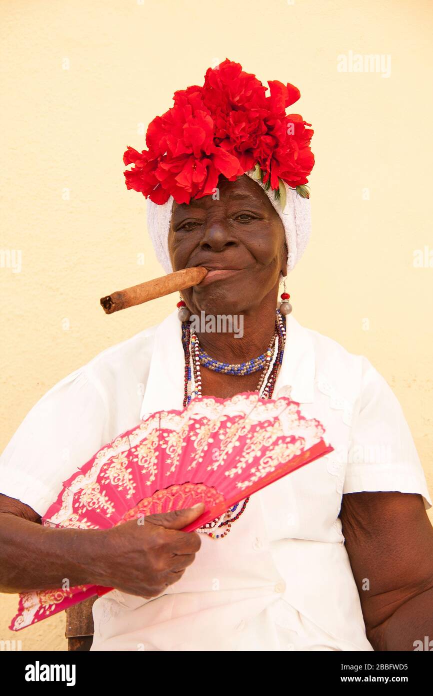 LA HAVANE, CUBA - 29 MARS 2017: Portrait d'une vieille femme noire dans des vêtements typiques de la Havane fume un grand cigare cubain sur un mur jaune pastel Banque D'Images