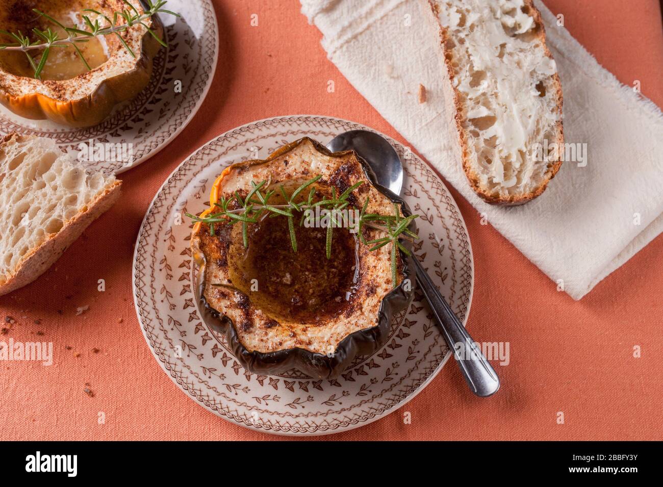 Courge d'orne cuite au four avec des tranches de sucre brun et des épices garnies de romarin et de pain beurré sur des assiettes Banque D'Images