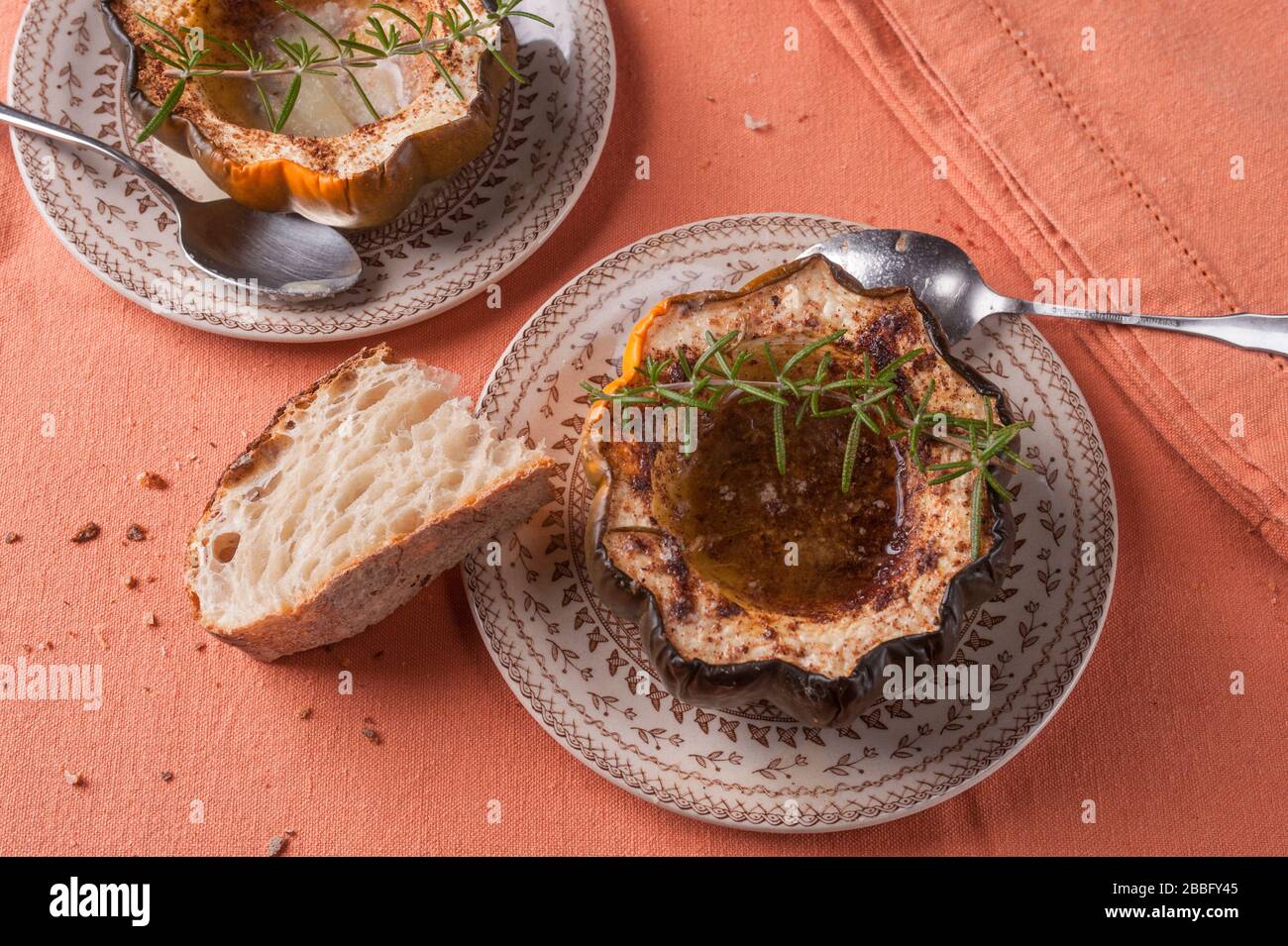 Courge d'orne cuite au four avec des tranches de sucre brun et des épices garnies de romarin et de pain beurré sur des assiettes Banque D'Images