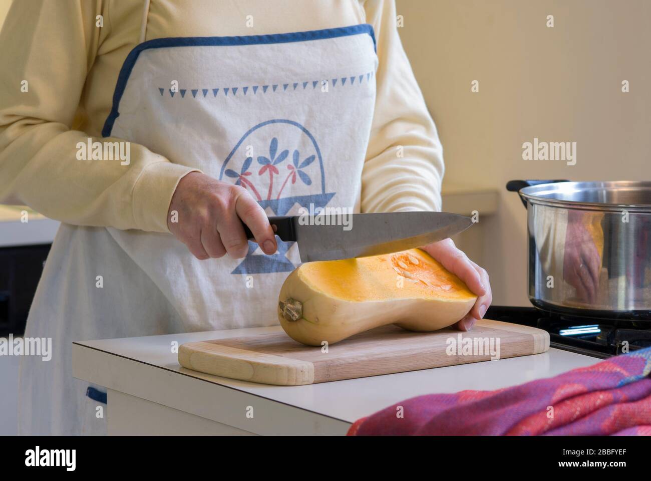 Femme dans la cuisine avec four brûleur de table de cuisson au gaz coupant le courge musquée pour faire de la soupe Banque D'Images