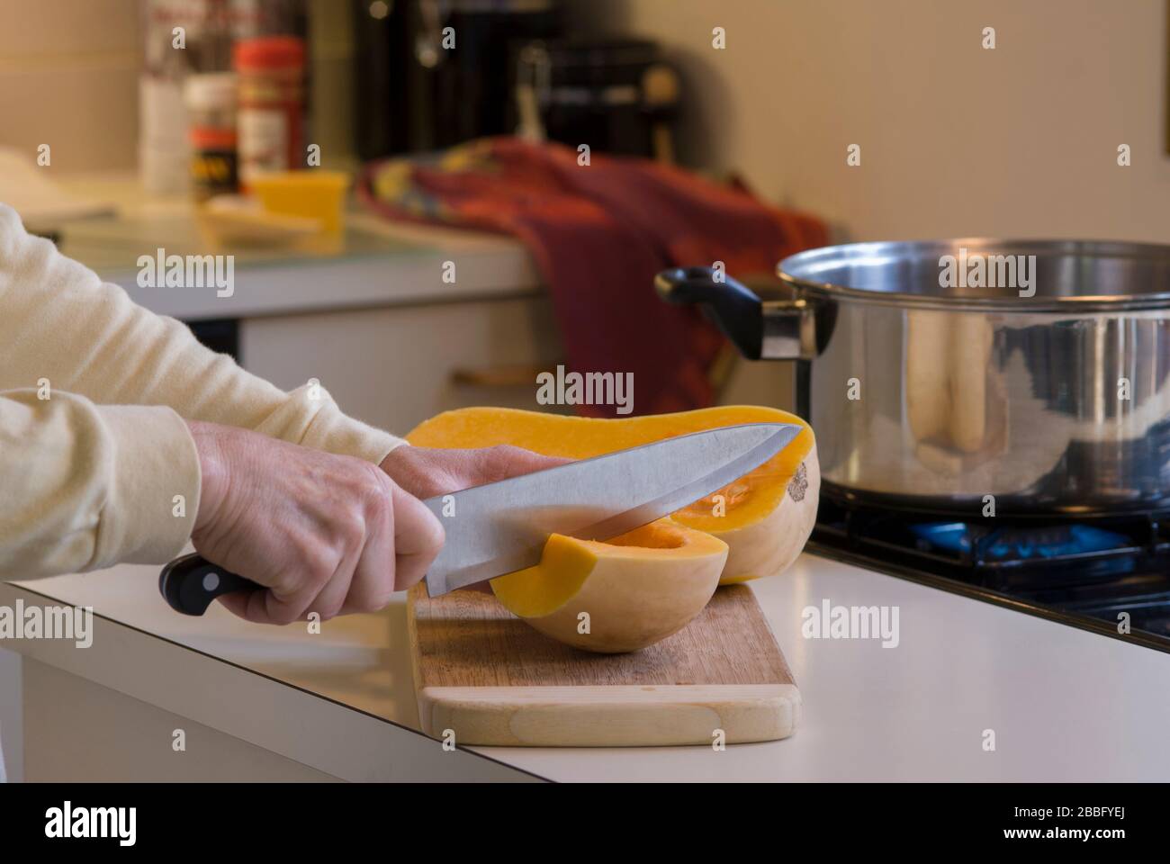 Femme coupant le courge musquée sur planche à découper en bois dans la cuisine à côté de la table de cuisson à gaz à quatre brûleurs pour soupe de courge musquée Banque D'Images