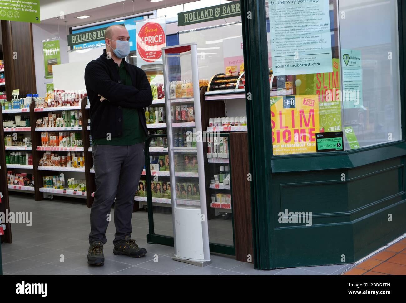 Un vendeur se tient à l'entrée du magasin Holland et Barrett portant un masque en raison de la pandémie de coronavirus au Royaume-Uni Banque D'Images