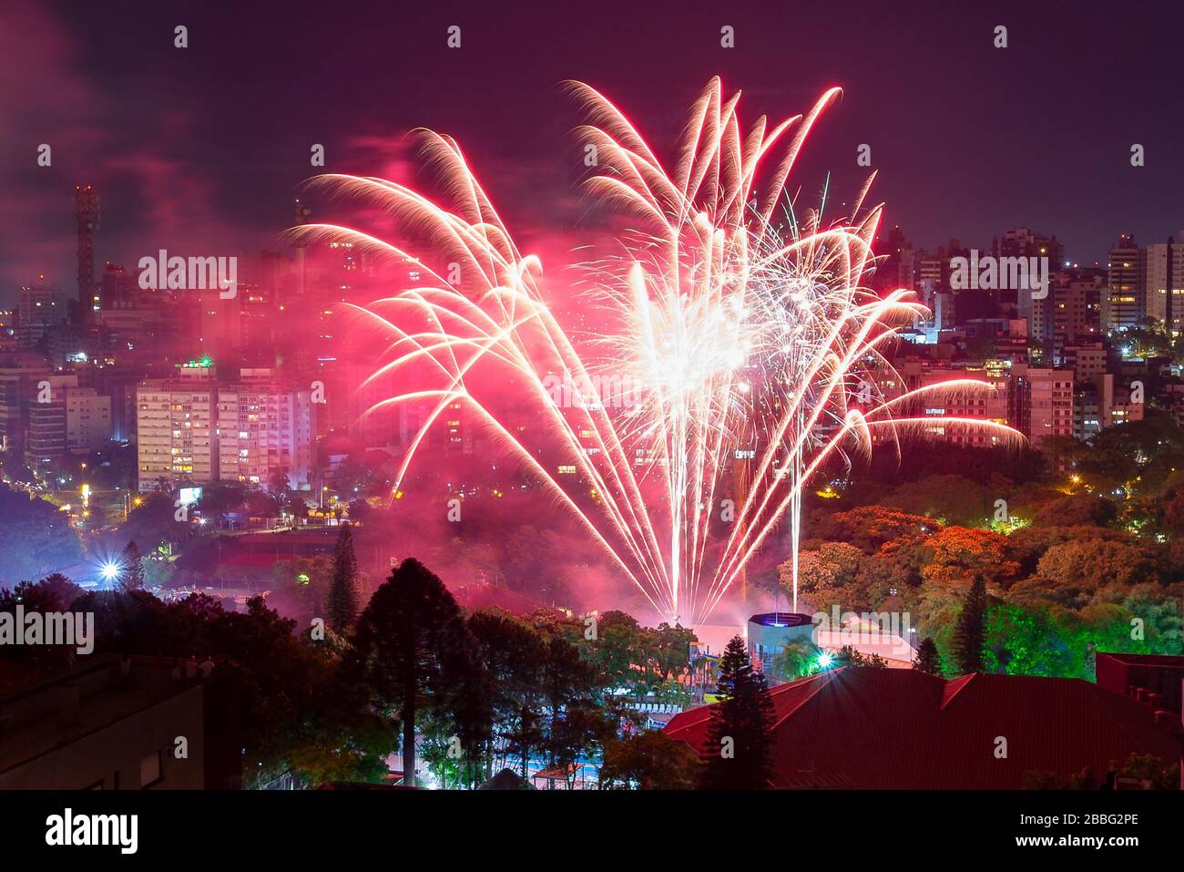 Célébration du nouvel an avec feux d'artifice devant les gratte-ciel de Porto Alegre, Brésil illuminé la nuit. Bâtiments résidentiels et parc avec arbres. Banque D'Images