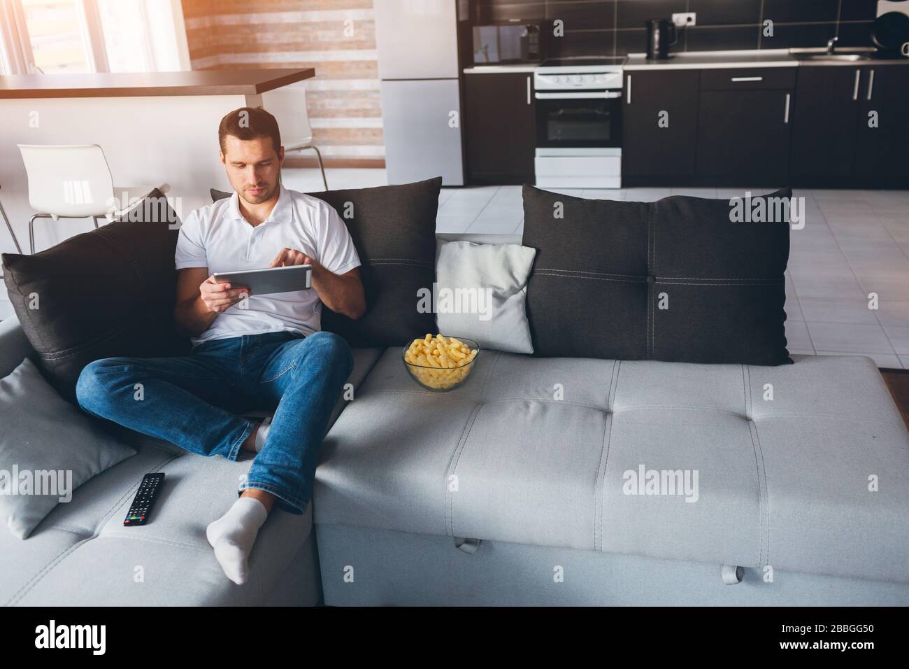 Jeune homme regarder la télévision dans son propre appartement.  Asseyez-vous seul sur le canapé et travaillez sur la tablette. Écran  tactile. Travail à distance à la maison. Seul dans la chambre concentré