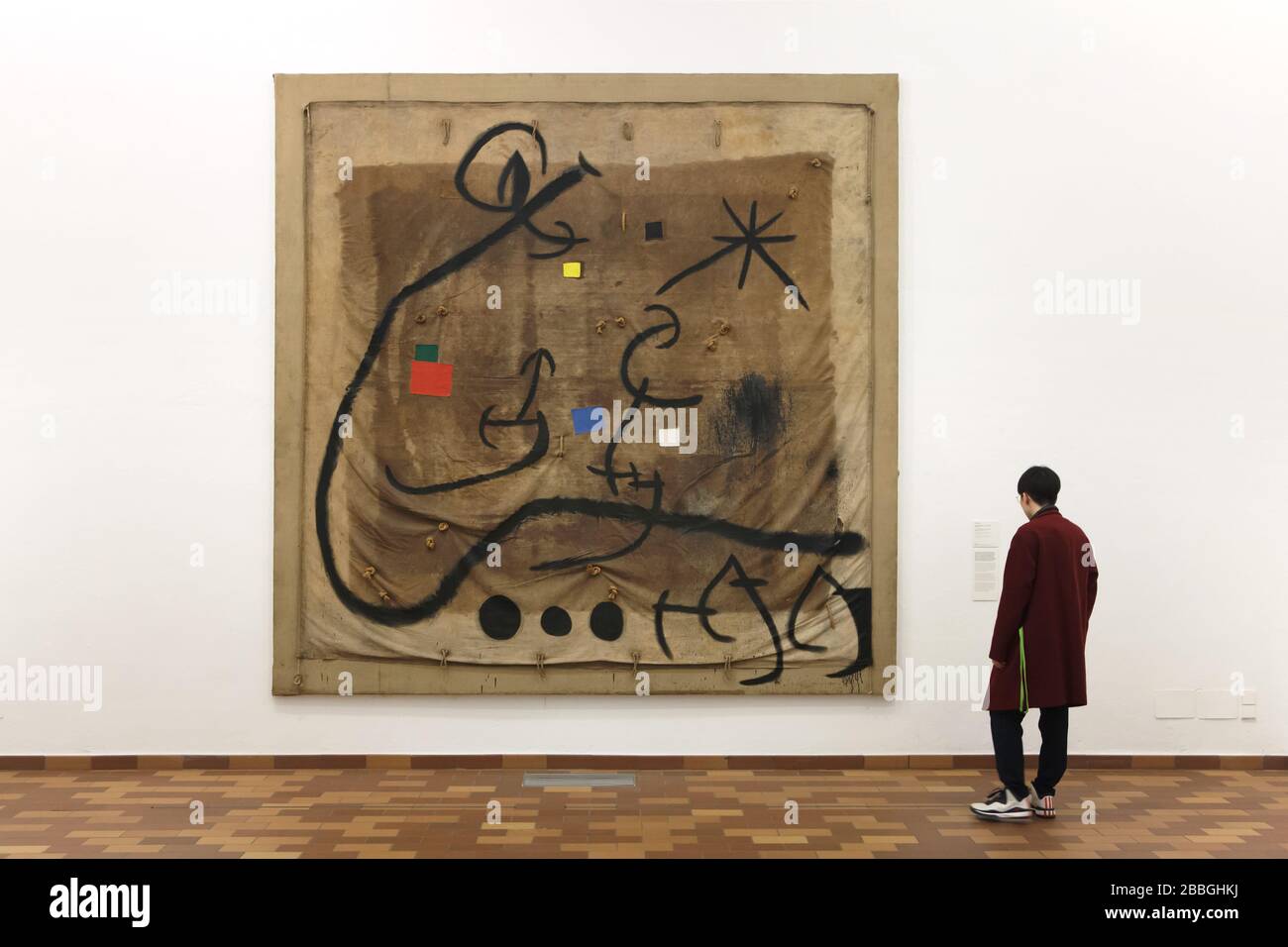Visiteur devant la peinture par le peintre moderniste espagnol Joan Miró intitulée 'Femme encerclée par un vol d'oiseau dans la nuit' (1968) affichée dans la Fundació Joan Miró (Fondation Joan Miró) à Barcelone, Catalogne, Espagne. L'œuvre est peinte sur le robinet utilisé pour transporter les raisins pendant la récolte. Banque D'Images