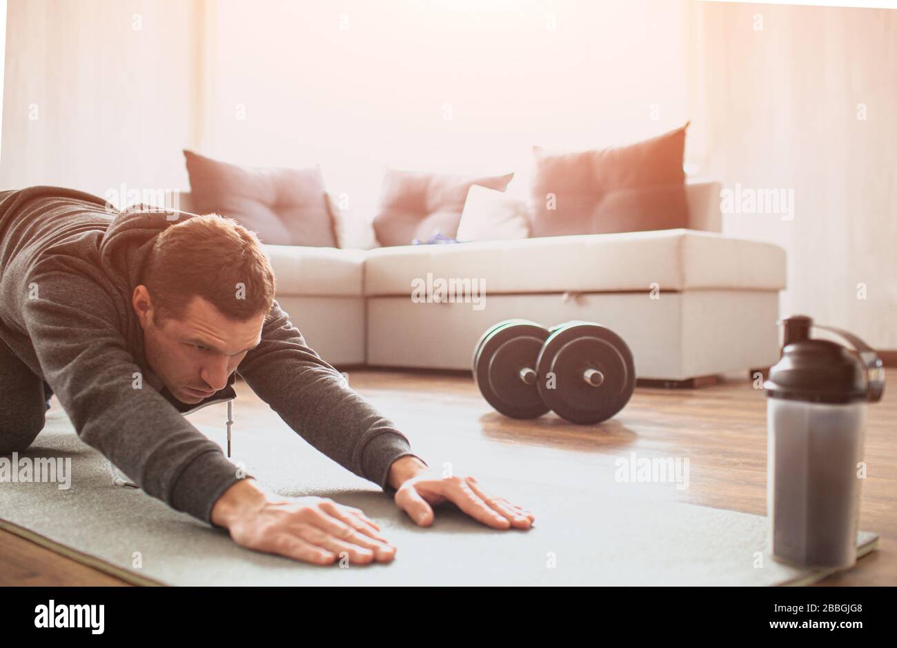 Jeune homme ordinaire va pour le sport à la maison. Couper la vue du débutant gars qui étire son corps et tirer les mains de fard sur le tapis. Amélioration de la forme du corps. Homme réel Banque D'Images