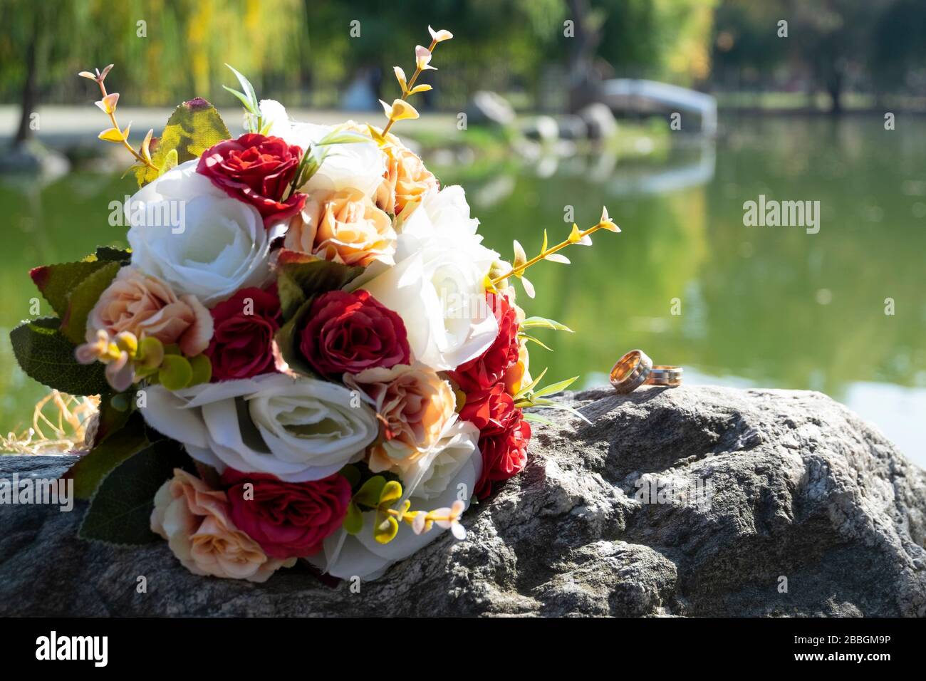 Le bouquet de mariage et les anneaux d'engagement se tiennent sur un rocher. Il y a une vue parfaite derrière les objets, le lac et les arbres. Banque D'Images