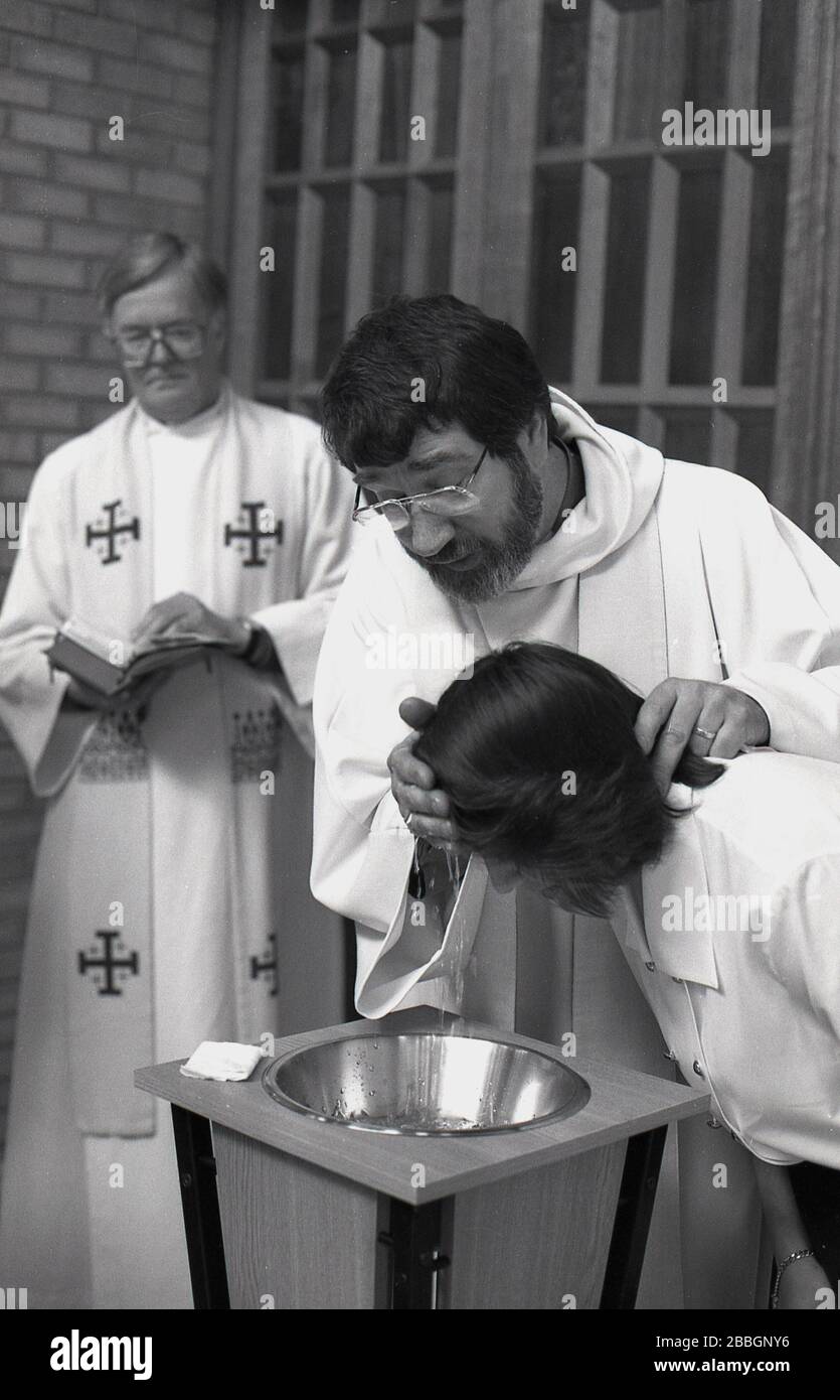 Années 1970, historique, à l'intérieur d'une église, une femme se fait baptiser, comme un prêtre robotisé mouille sa tête, Sud de Londres, Angleterre, Royaume-Uni. Le baptême est un rite chrétien d'admission, un sacrement, une ordonnance de Jésus-Christ. Banque D'Images