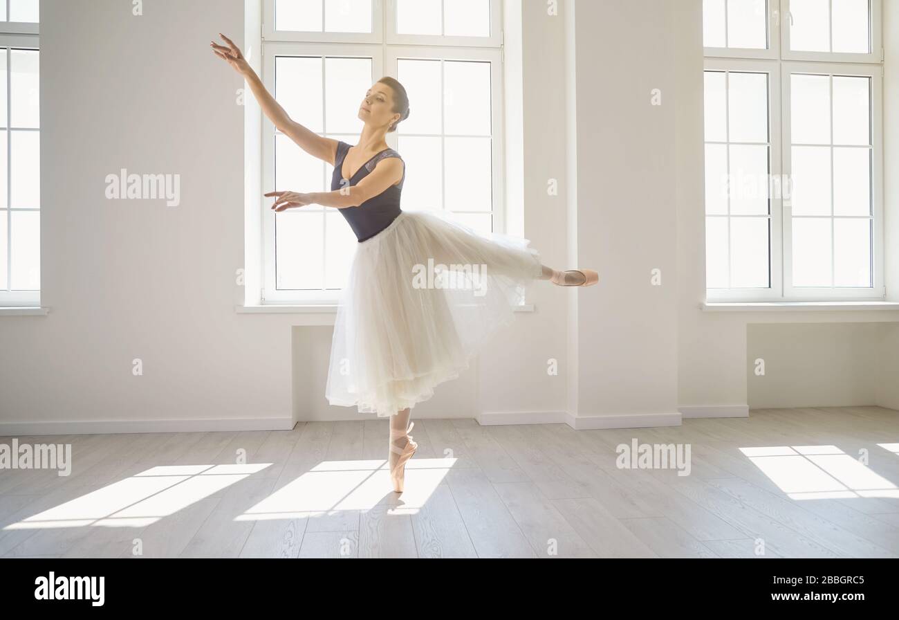 Ballerine. La jeune danseuse de ballet élégante répète une performance dans un studio de classe blanche avec des fenêtres. Banque D'Images