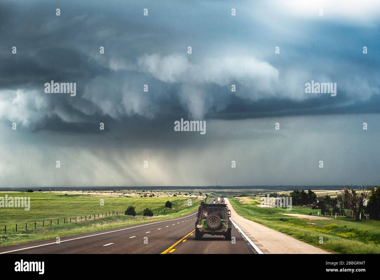 Le nuage d'entonnoir menace de laisser tomber la tornade sur la route devant la jeep sur l'autoroute rurale du Kansas États-Unis Banque D'Images
