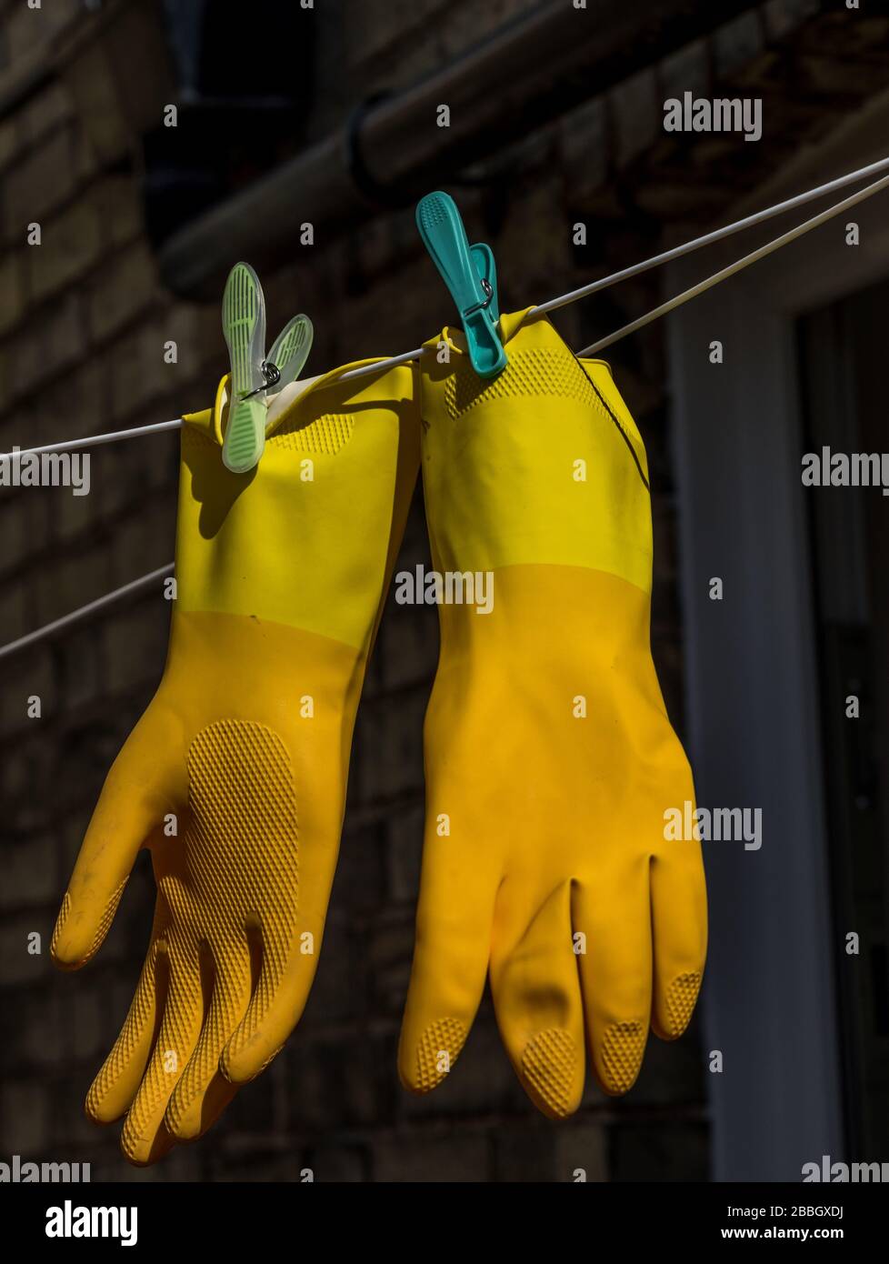 Une paire de gants de protection en caoutchouc jaune marigold est fixée sur une ligne de vêtements Banque D'Images