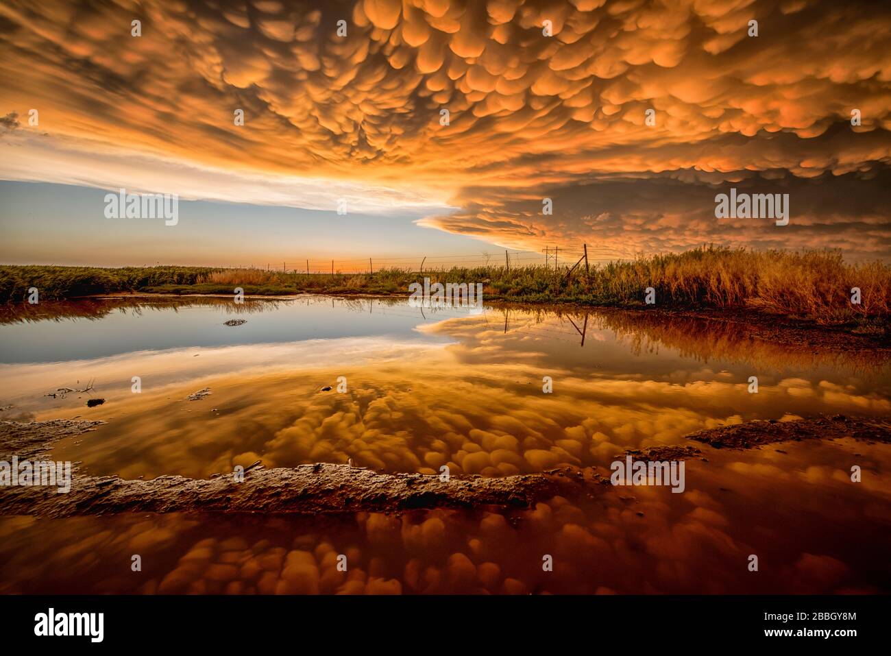 Coucher de soleil sur un étang avec un reflet parfait de manmatus orange brillant pendant que la tempête passe à Dodge City Kansas États-Unis Banque D'Images