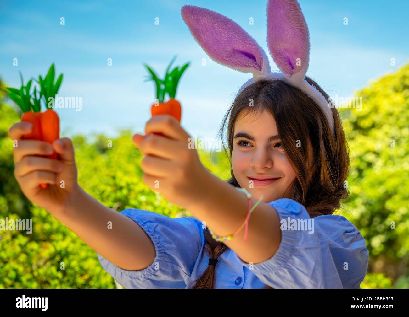 Portrait d'une douce petite fille vêtue d'un lapin, jouant avec des carottes, s'amuser à l'extérieur en journée ensoleillée de printemps, passer Pâques à l'extérieur Banque D'Images