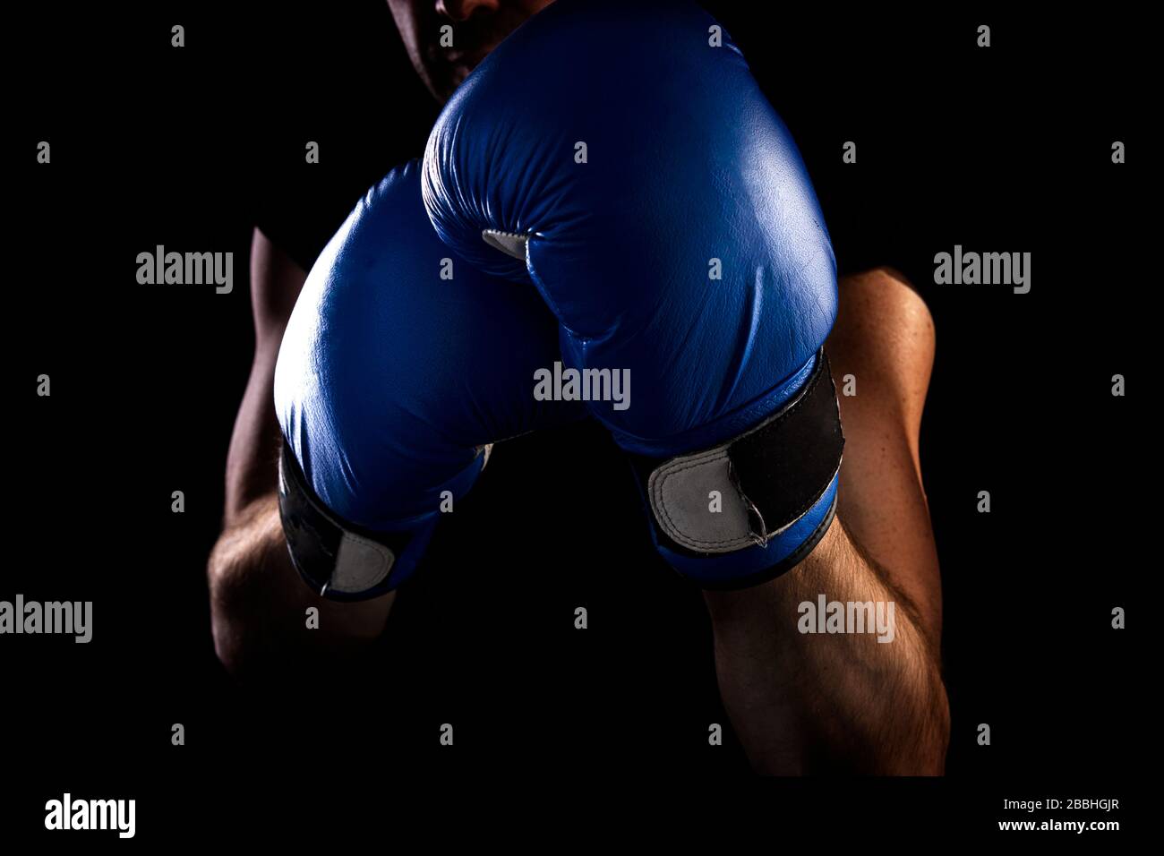 l'homme se tient en position de boxe, tient des gants de boxe bleus sur ses mains, fond sombre Banque D'Images