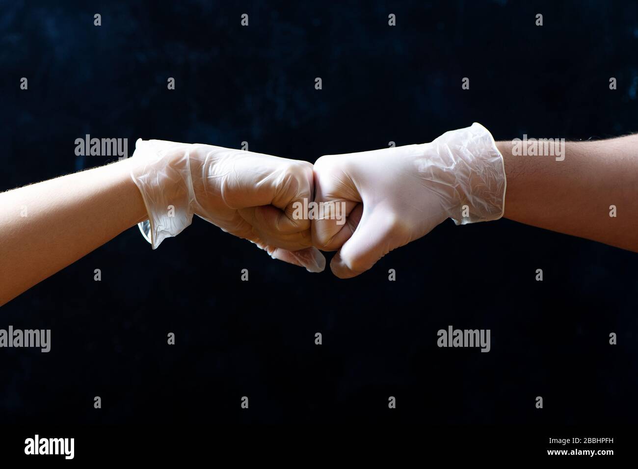 Les mains d'amis dans des gants médicaux se saluent l'un l'autre avec un coup de poing sur fond noir. Banque D'Images