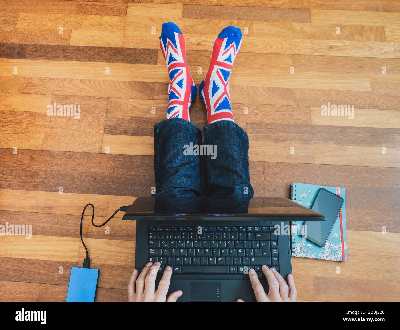 Homme portant une chaussette drapeau Jack Union assise sur parquet avec ordinateur portable. Travailler de chez soi, isolement de soi, distanciation sociale, Coronavirus... concept Banque D'Images