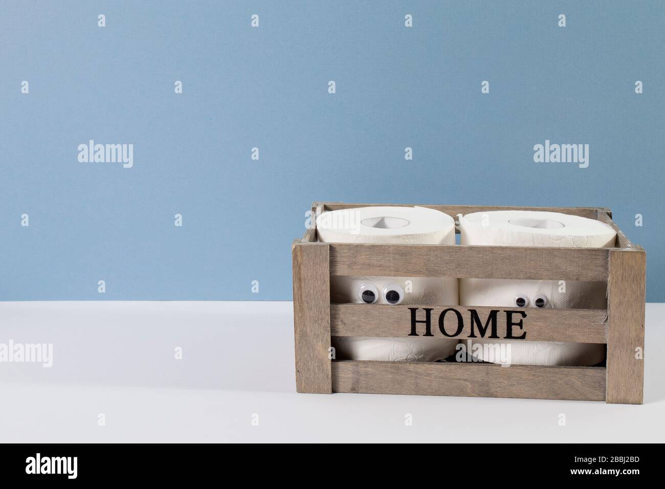 Deux rouleaux de papier toilette avec yeux artificiels dans une boîte en bois avec l'inscription Home sur le fond bleu gris Banque D'Images