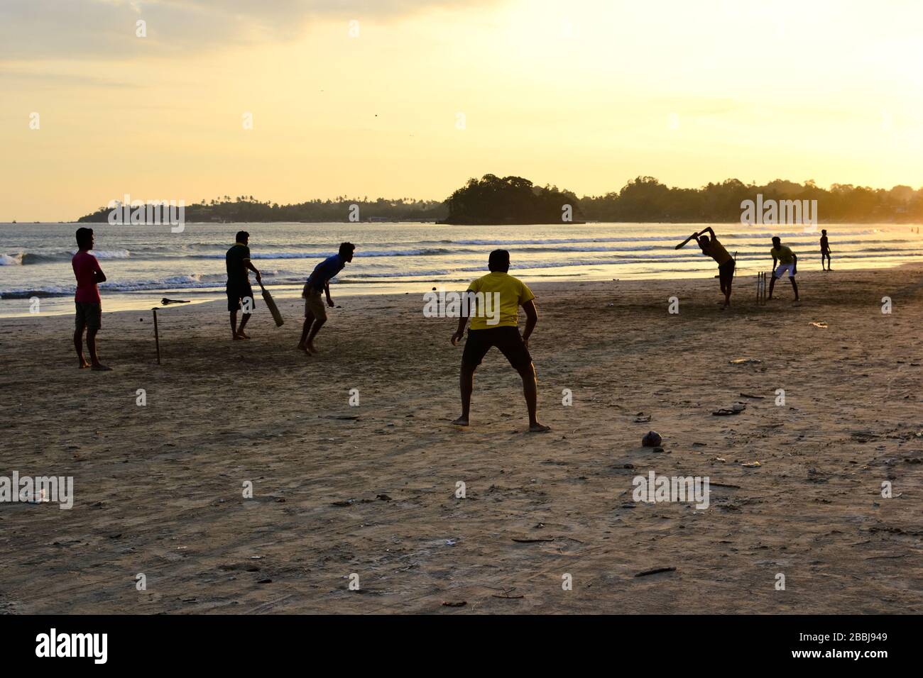 Jeunes garçons jouant au cricket sur une plage. Silhouettes de jeunes garçons s'amuser sur la plage du Sri Lanka. Coucher de soleil doré avec rayons de soleil à Weligama Banque D'Images