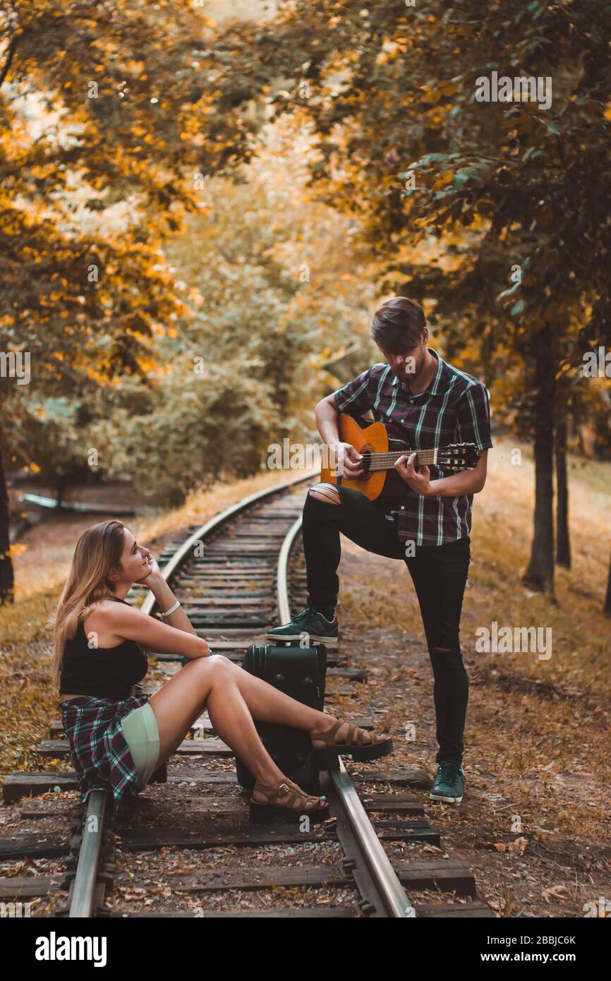 Un jeune couple d'amoureux a manqué le train. Jouer de la chanson avec de la guitare sur les rails dans la forêt d'automne en attendant le prochain train. Banque D'Images