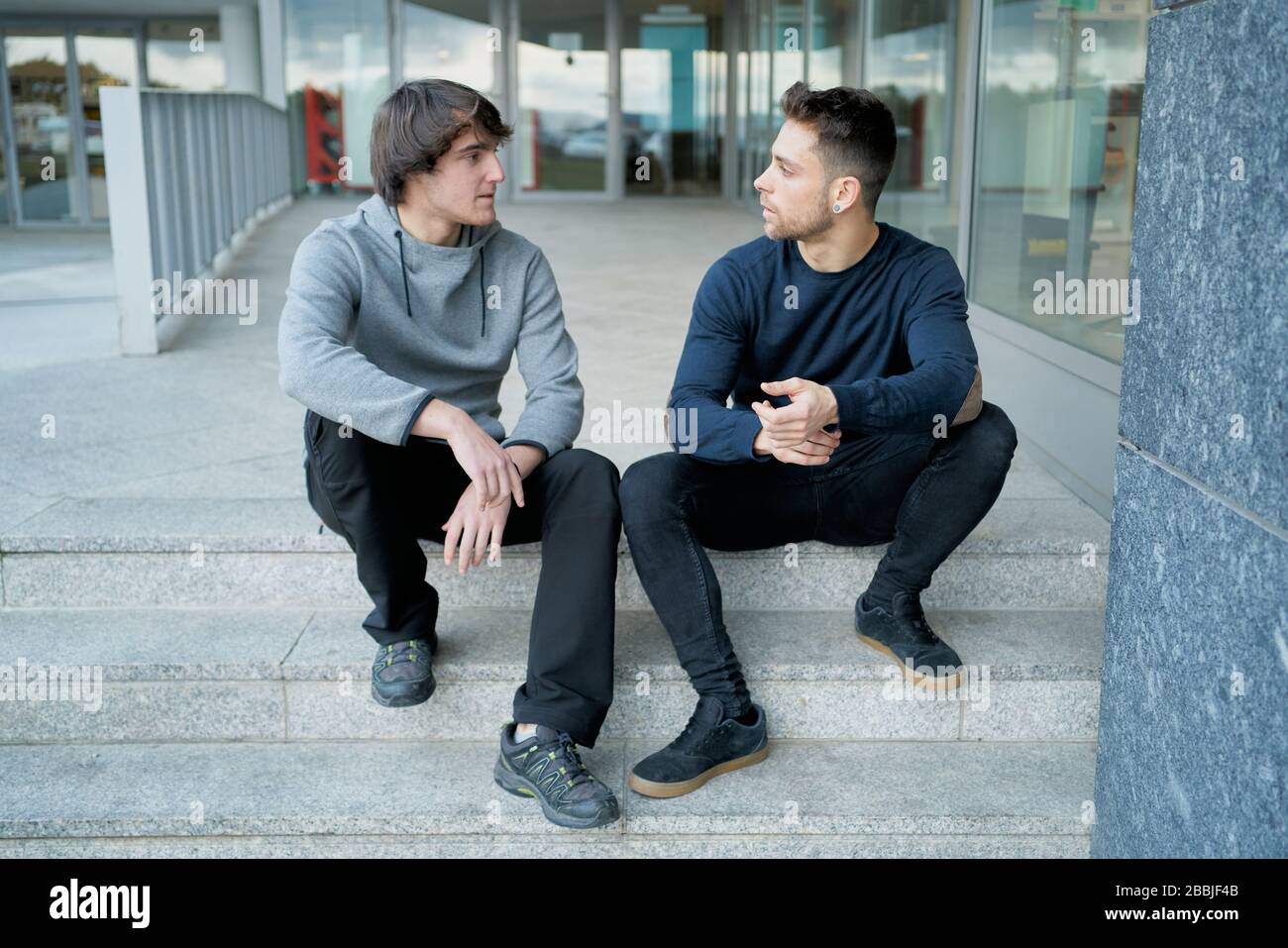 Vue de face de deux jeunes hommes qui parlent assis sur un escalier de la ville Banque D'Images