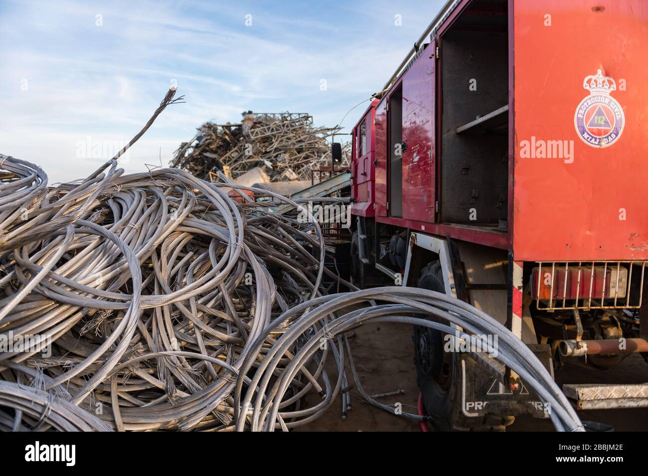 Un camion de protection civile à côté d'une pile de bobines de câble métallique dans une cour en junkyard Banque D'Images