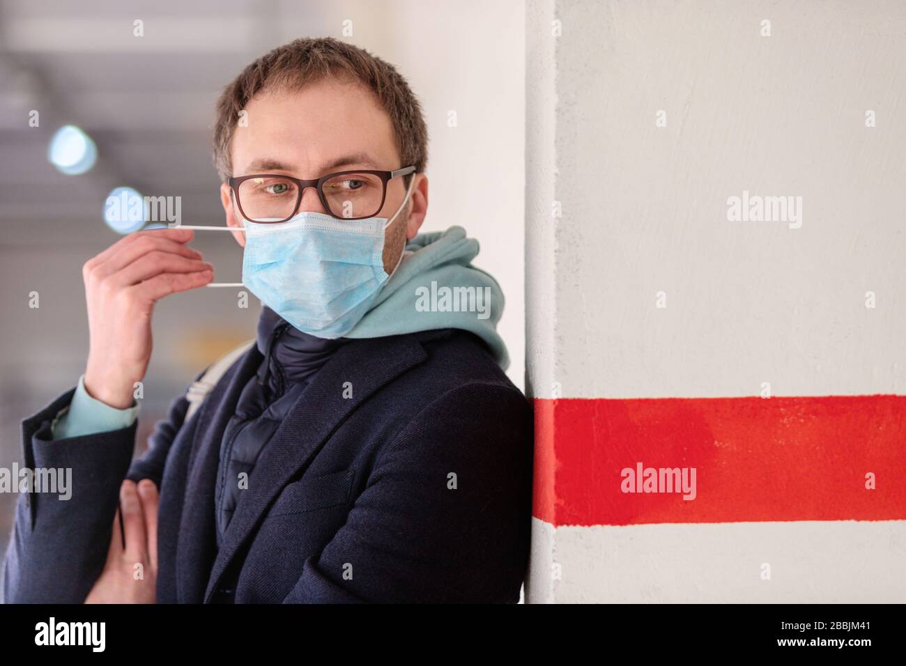 Homme européen malade dans des lunettes portant un masque médical de protection, debout près du mur avec une ligne rouge. Épidémie de grippe, allergie à la poussière et au pollen, protection Banque D'Images