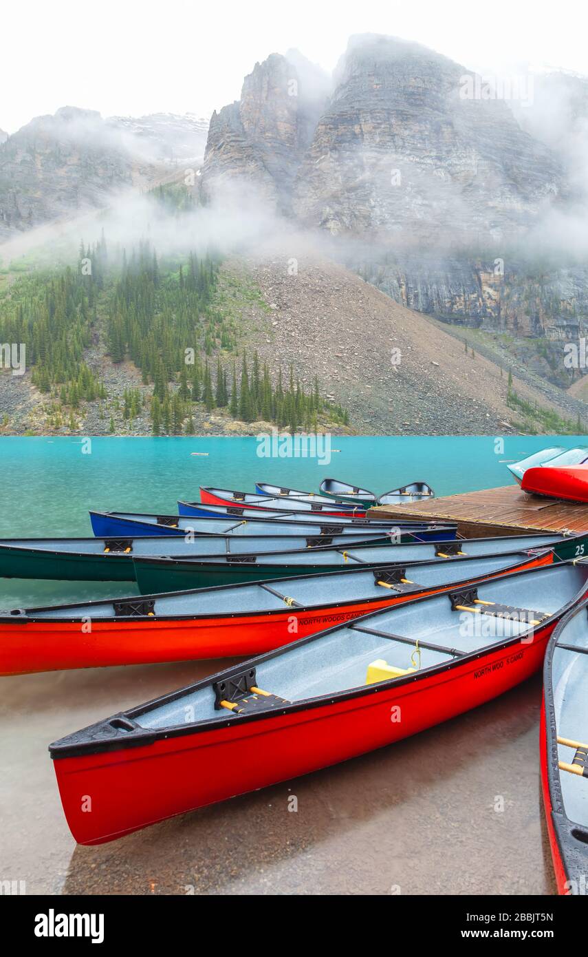Des canoës colorés au lac Moraine, parc national Banff, Alberta, Canada, lors d'une journée d'été pluvieuse. Banque D'Images