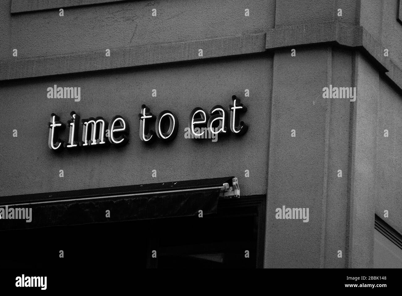 Un panneau sur un bâtiment qui lit "le temps de manger" en noir et blanc Banque D'Images