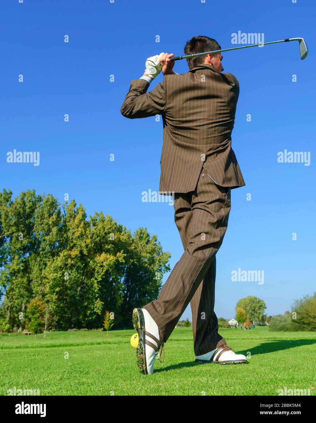 Homme en tenue d'affaires jouant au golf dans l'après-midi Banque D'Images