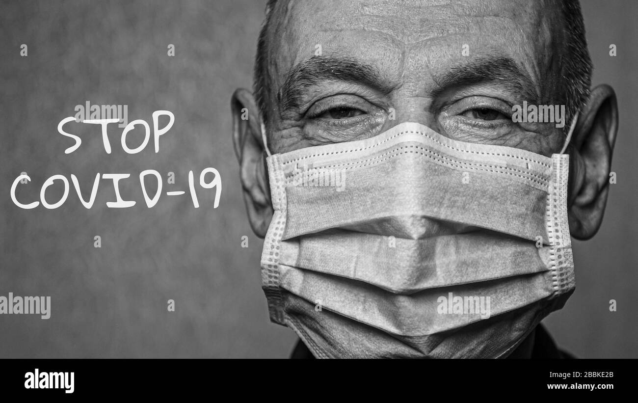 Un homme âgé dans un masque médical avec une inscription STOP COVID-19. Groupe de risques. Photo en noir et blanc. Concept de COVID-19. Maladie du coronavirus. Fermer Banque D'Images