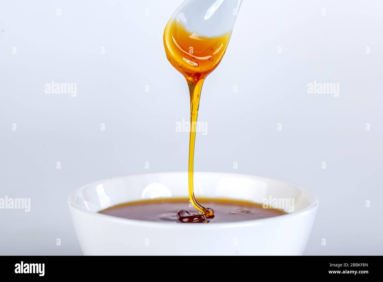 le miel s'écoule de la cuillère en céramique à la cuvette en céramique Banque D'Images