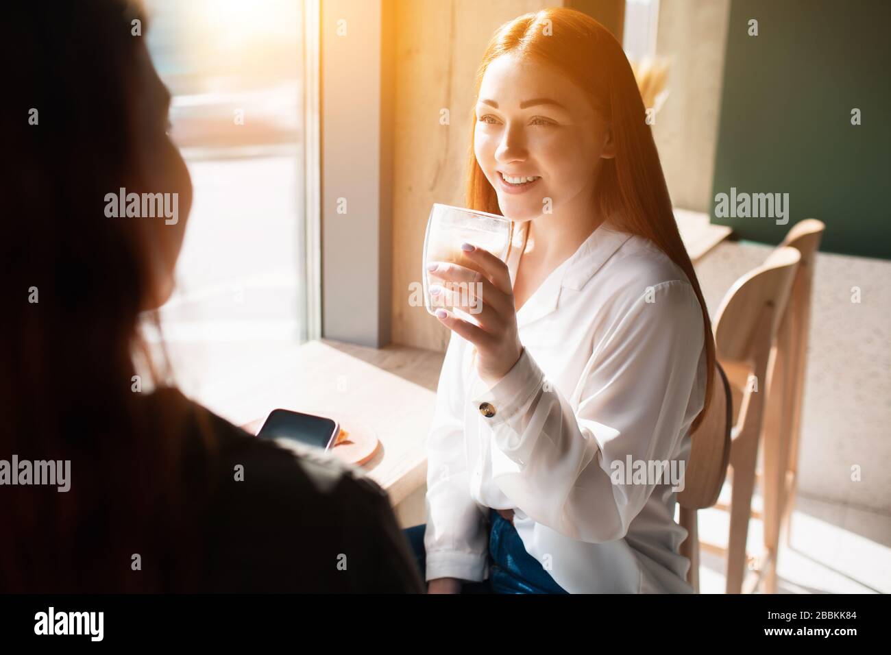 La jeune femme tient une tasse de café et parle avec son ami. Le modèle féminin boit du café et se trouve dans un café Banque D'Images