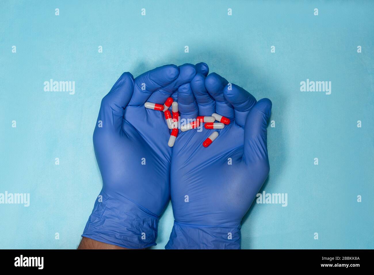 Les mains du médecin dans des gants médicaux bleus sont étirées vers l'avant et tenant une pilule rouge et blanche. Banque D'Images