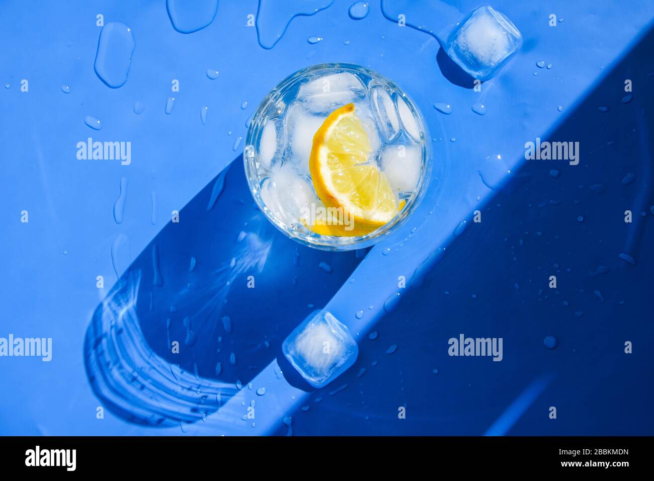 Un verre d'eau rafraîchissante avec de la glace et du citron sur un fond bleu. Concept de chaleur, frais. Lumière naturelle. Couche plate, vue supérieure, espace de copie Banque D'Images