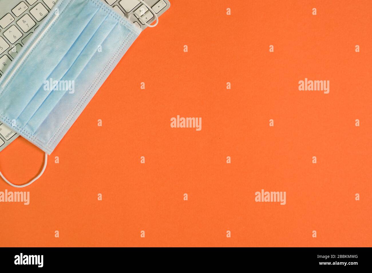Vue de dessus de la table de bureau de couleur orange avec clavier et masque chirurgical. Espace de copie. Banque D'Images