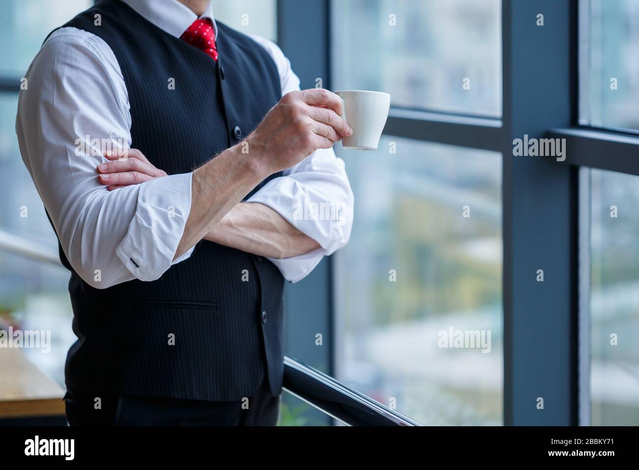 Sourire heureux directeur général pense à son développement de carrière réussi tout en se tenant avec une tasse de café dans sa main dans son bureau près de la Banque D'Images