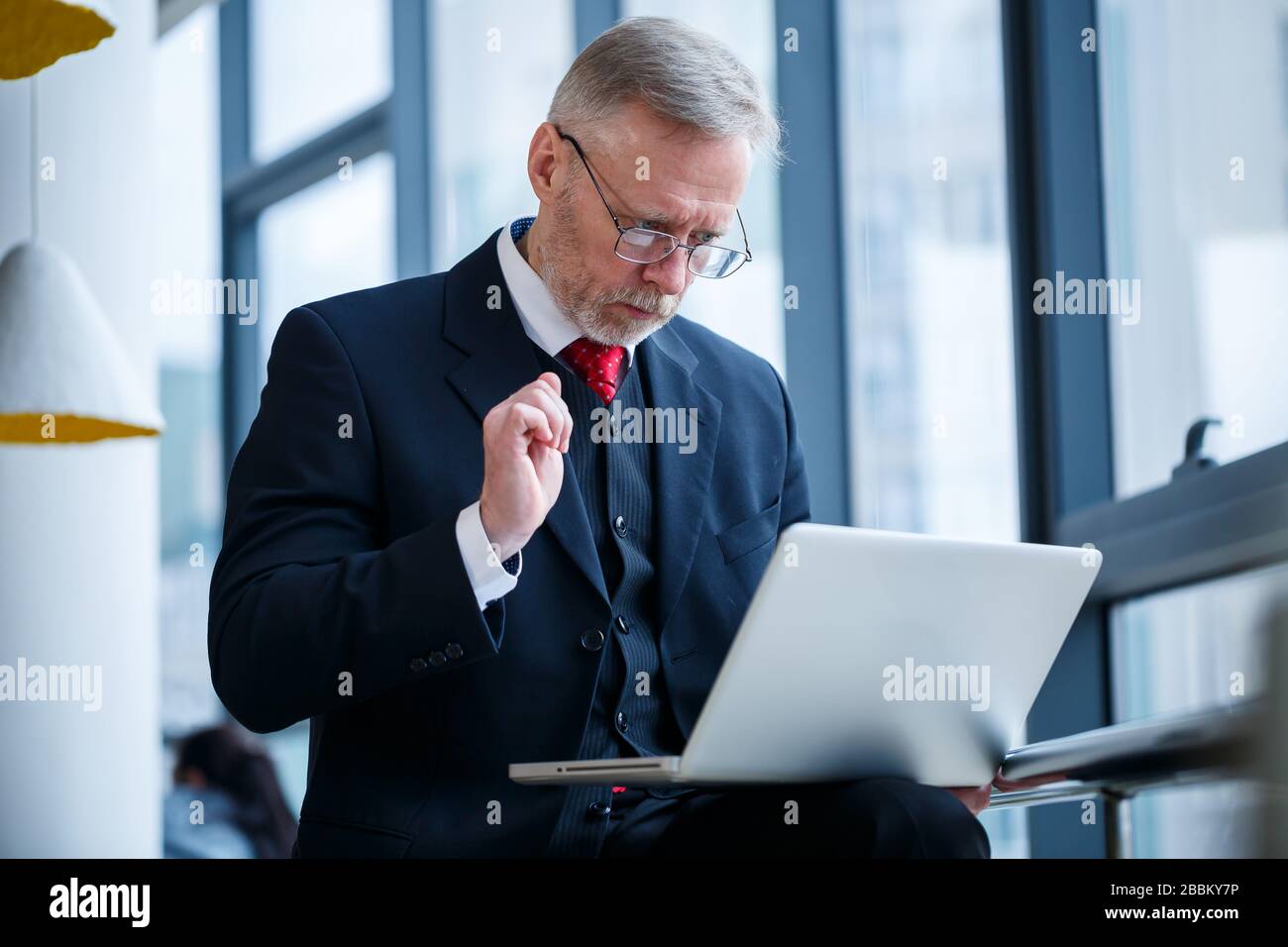 Sourire heureux directeur général pense à son développement de carrière réussi tout en se tenant debout avec un ordinateur portable dans son bureau près de l'arrière-plan d'une victoire Banque D'Images