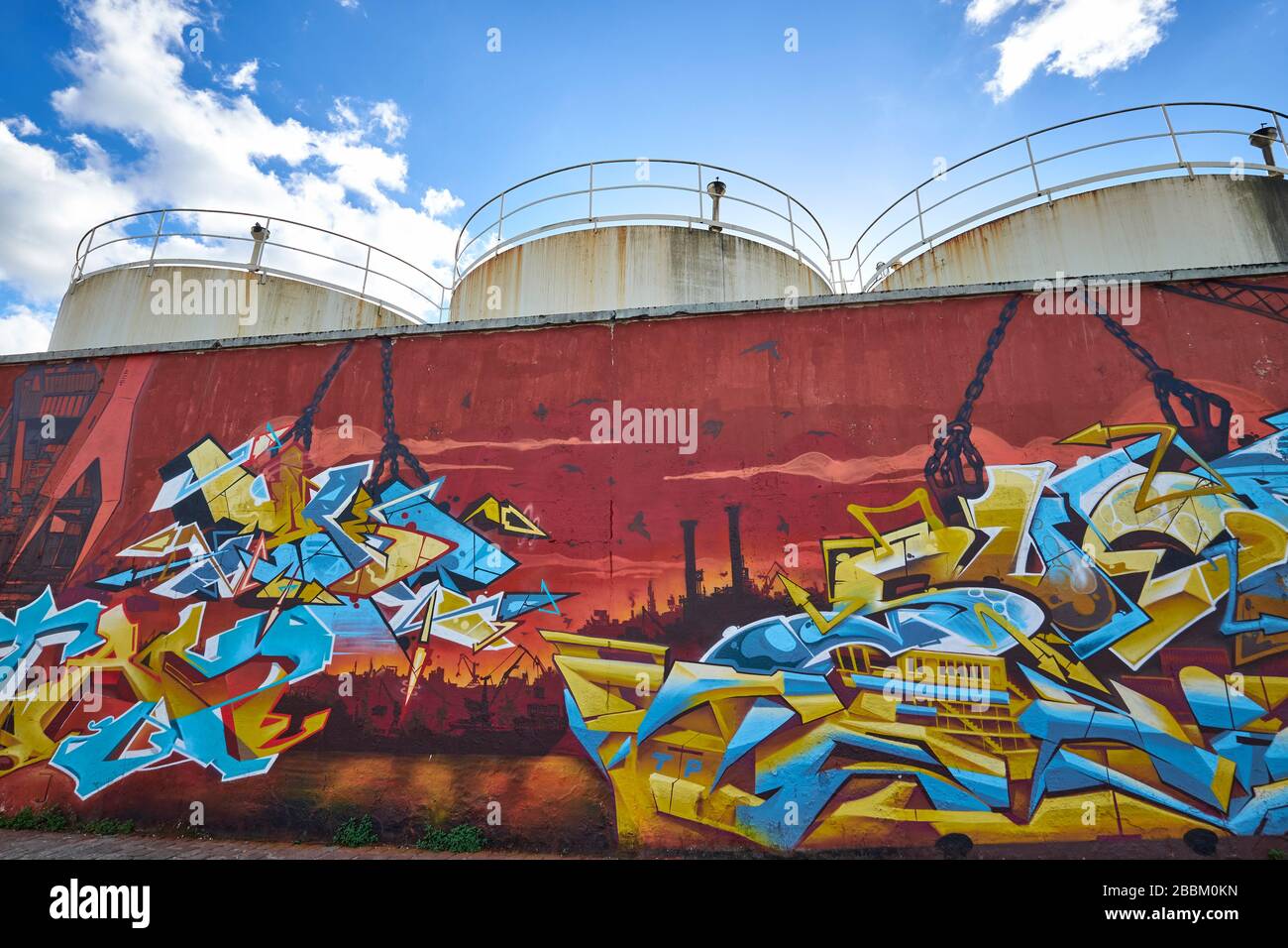 Graffitis peint sur un mur de pierre avec 3 réservoirs de stockage d'huile derrière au Quai de Sénégal dans la zone de réaménagement de Bacalan-Bassins à Flot, Bordeaux Banque D'Images