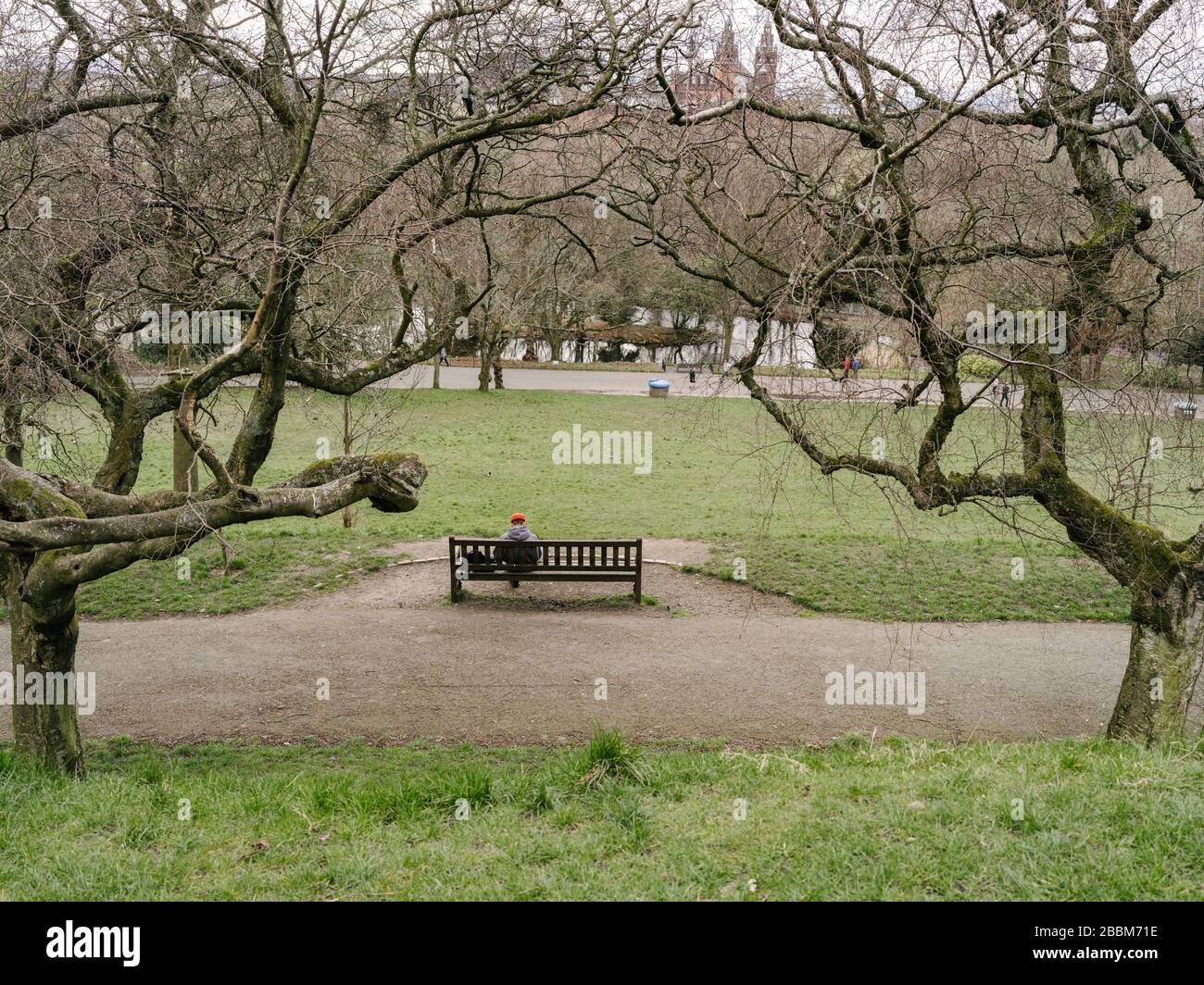 Homme avec Red Hat assis sur un banc de parc se distançant socialement pendant la pandémie de Coronavirus au Royaume-Uni. Banque D'Images