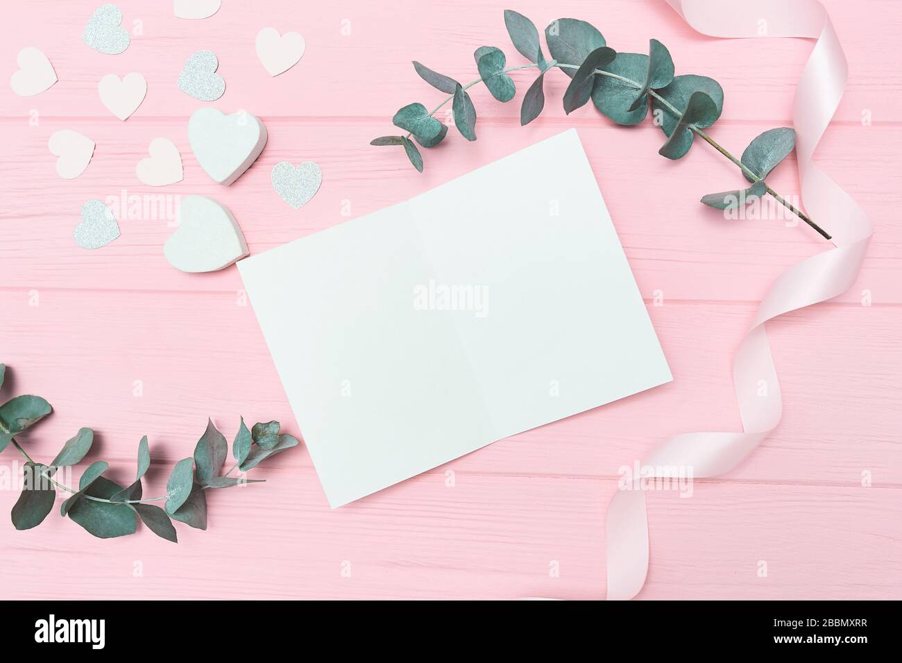 Valentines Day ou maquette de mariage scène avec carte vierge, de feuilles d'eucalyptus et de confettis Coeurs en papier cadre fond rose en bois, vide de l'espace pour votre Banque D'Images