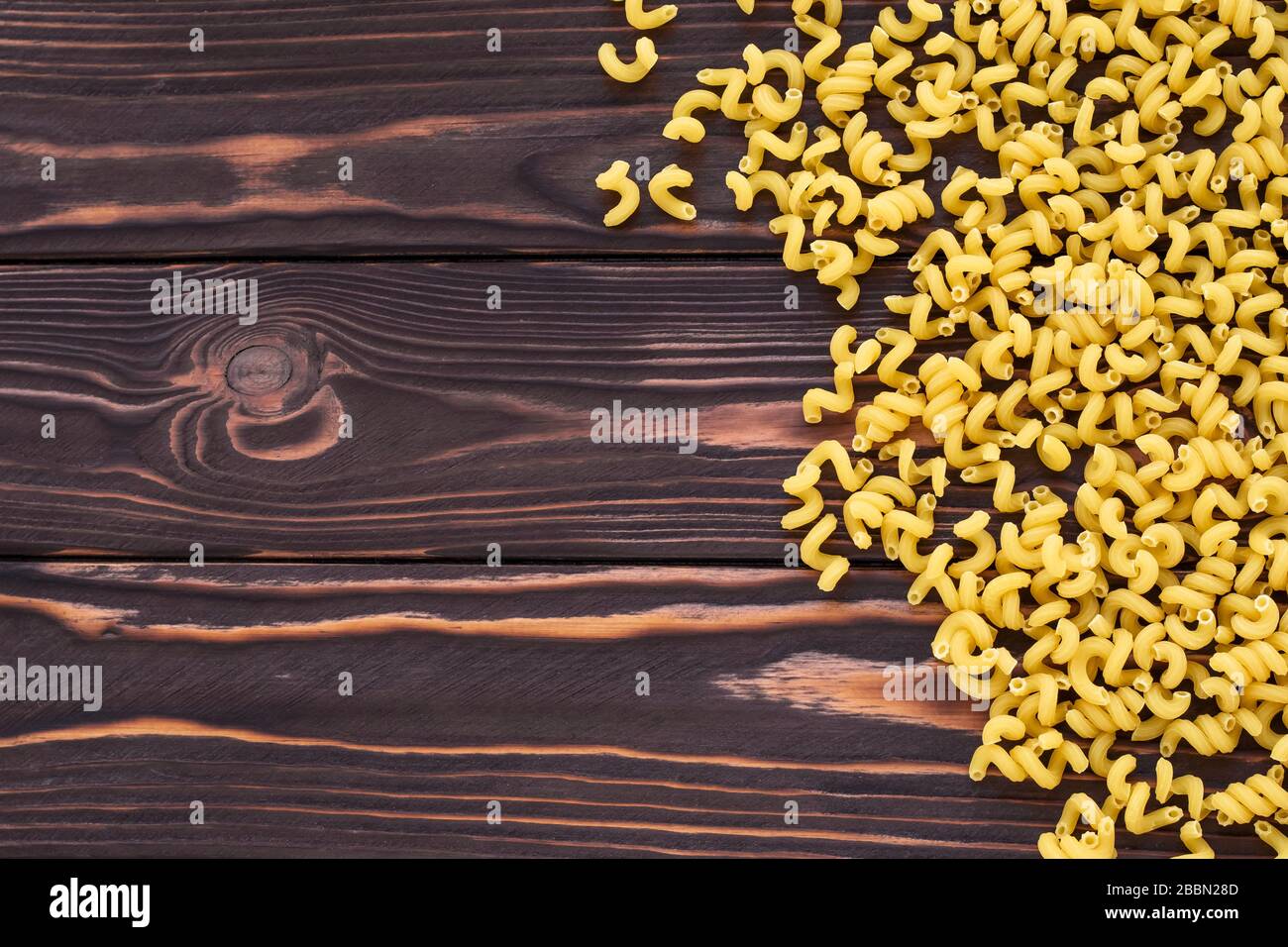 Fond en bois sombre abstrait avec pâtes jaunes. Cuisine italienne traditionnelle. Vue du dessus de la table. Modèle de macaroni. Décor culinaire, cadre alimentaire. EM Banque D'Images