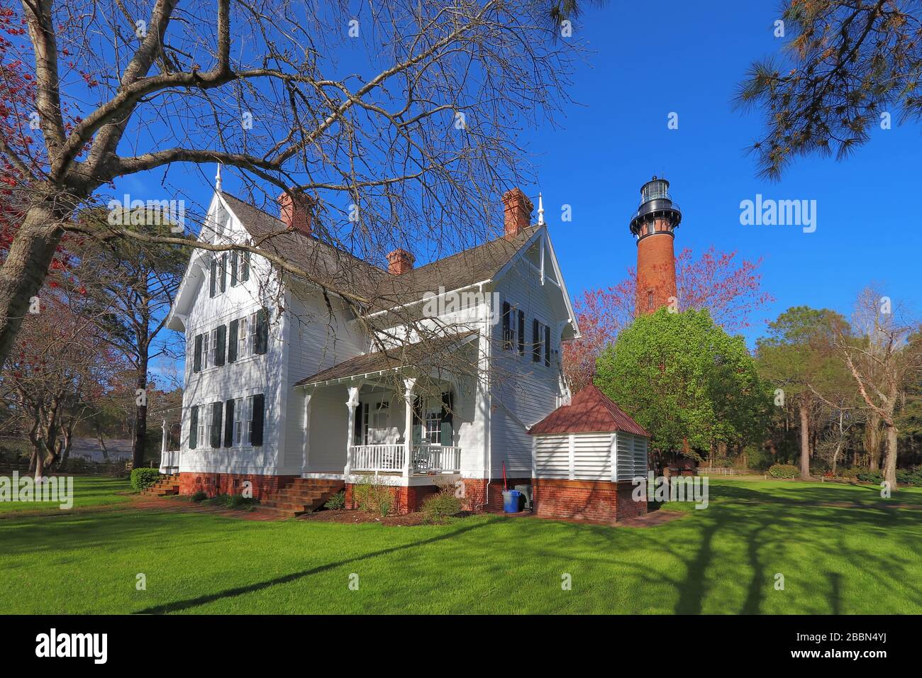 Les gardiens se trouvent devant la structure en briques rouges du phare de Currituck Beach, avec des arbres printaniers au parc du patrimoine de Currituck, près de Corolla Banque D'Images