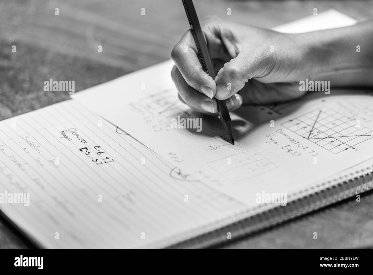 Main d'un enseignant tenant un crayon et écrivant une équation mathématique (formule) dans un manuel. Noir et blanc. Banque D'Images Main d'un enseignant tenant un crayon et écrivant une équation mathématique (formule) dans un manuel. Noir et blanc. Banque D'Images
