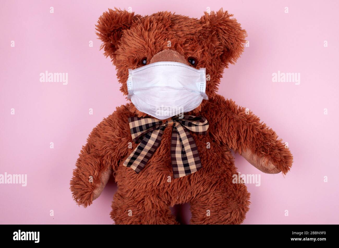 Ours en peluche avec masque facial médical sur fond rose clair Banque D'Images